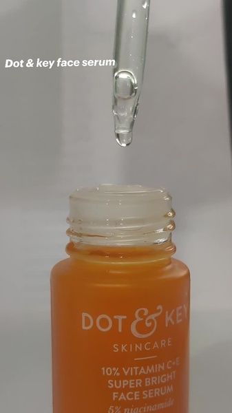 A close-up vertical shot showing a serum droplet falling from a glass pipette onto a brightly colored orange product bottle.